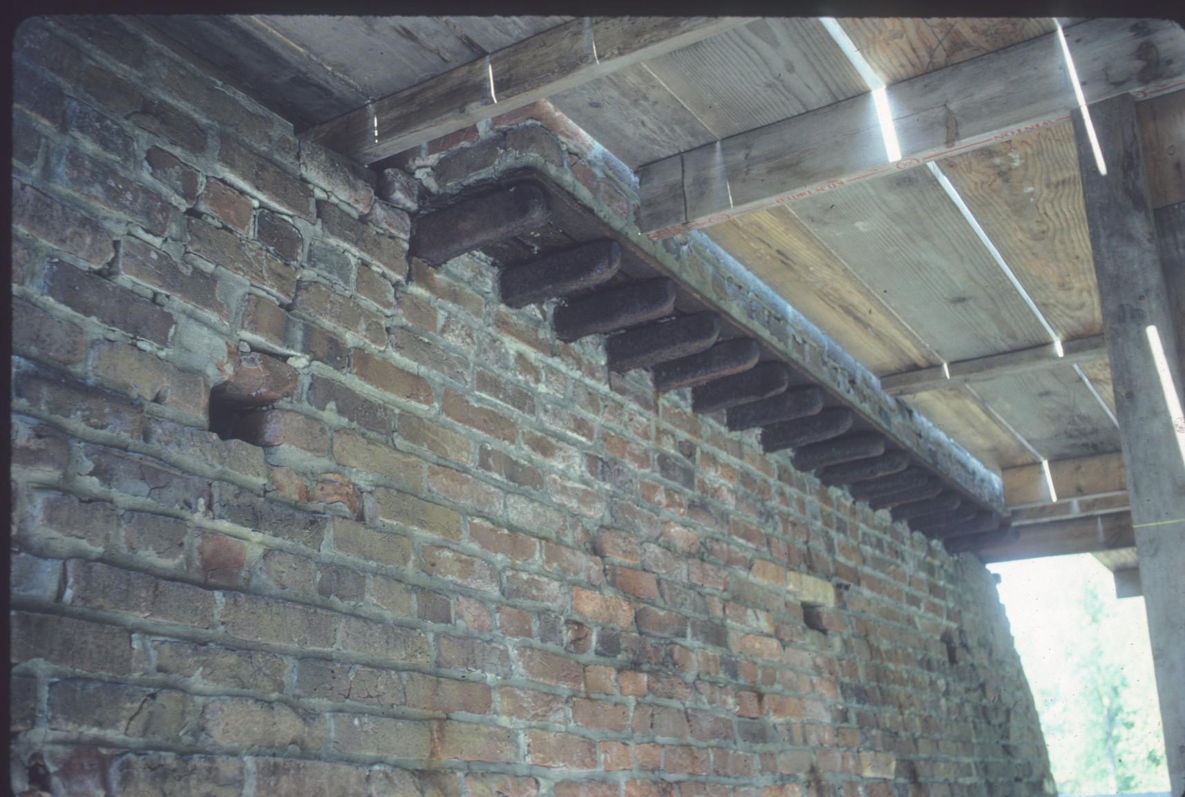 View of underside of wooden deck at brick furnace wall.  Iron pigs used as…