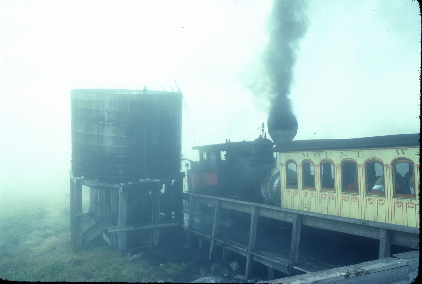 Train at summit by water tank in fog