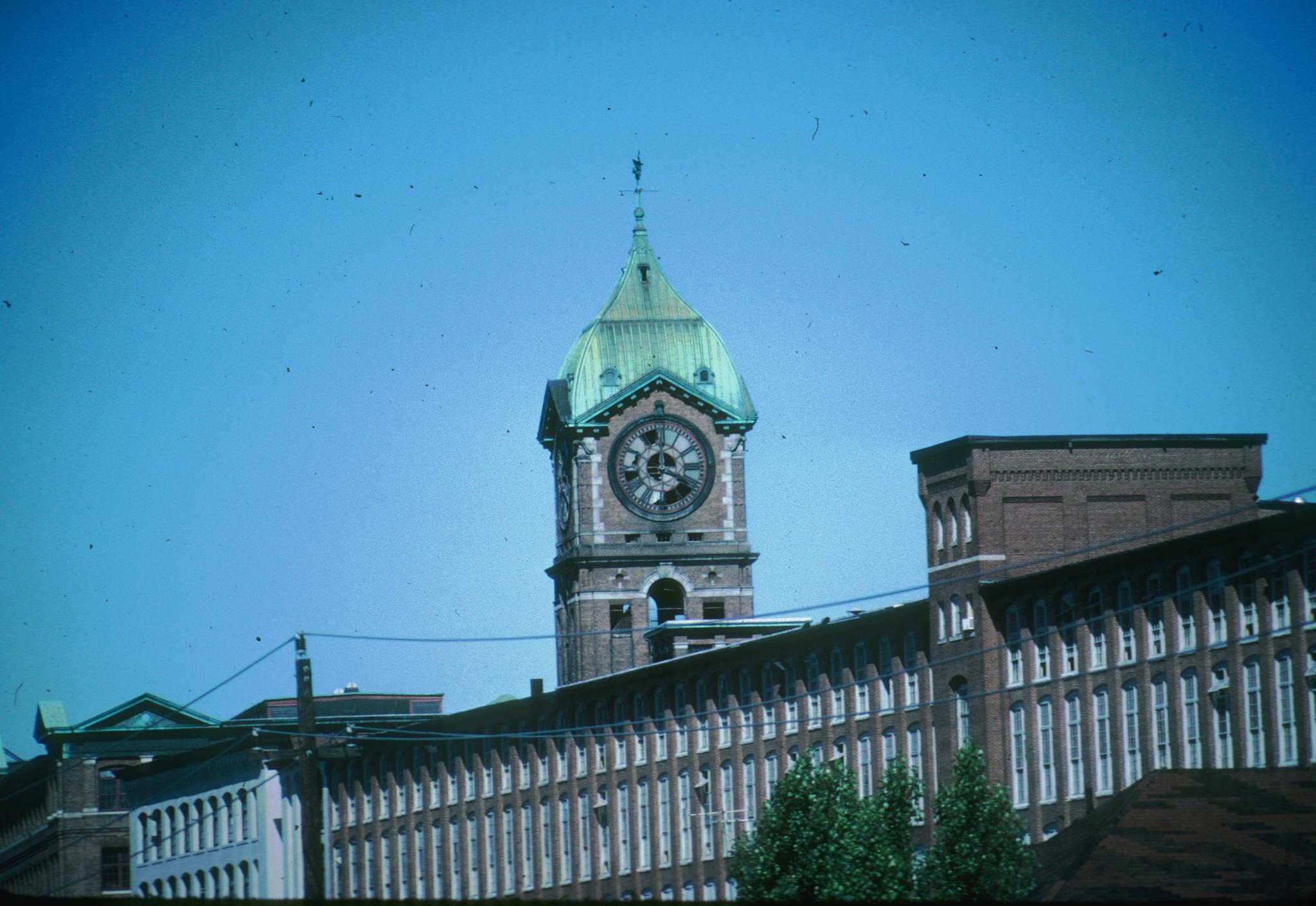 Photograph of Ayer Mill No. 1's clock tower.  The Wood Mill roofline is in…