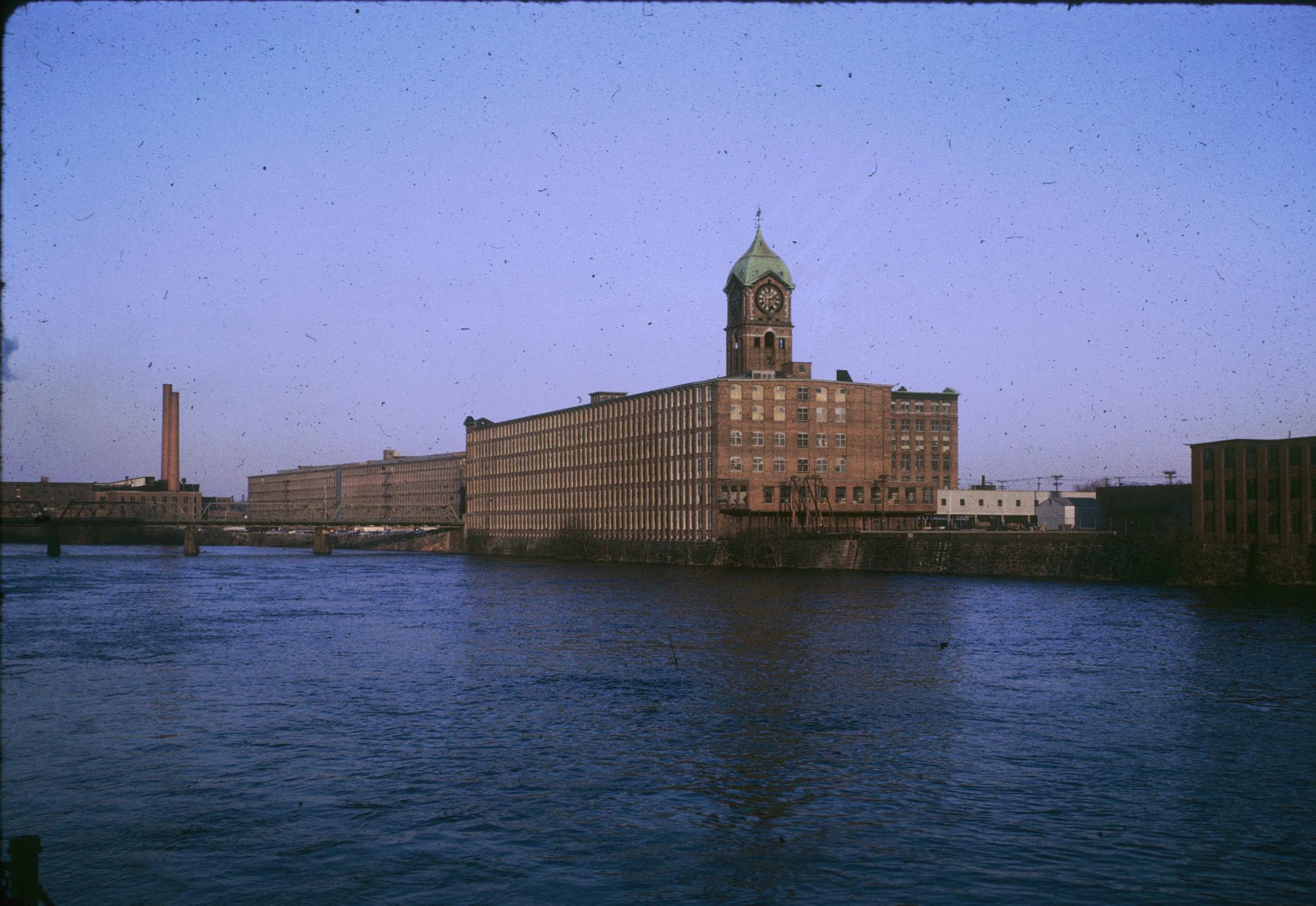 Photograph of the mill with the Merrimack River in the foreground and Wood Mill…