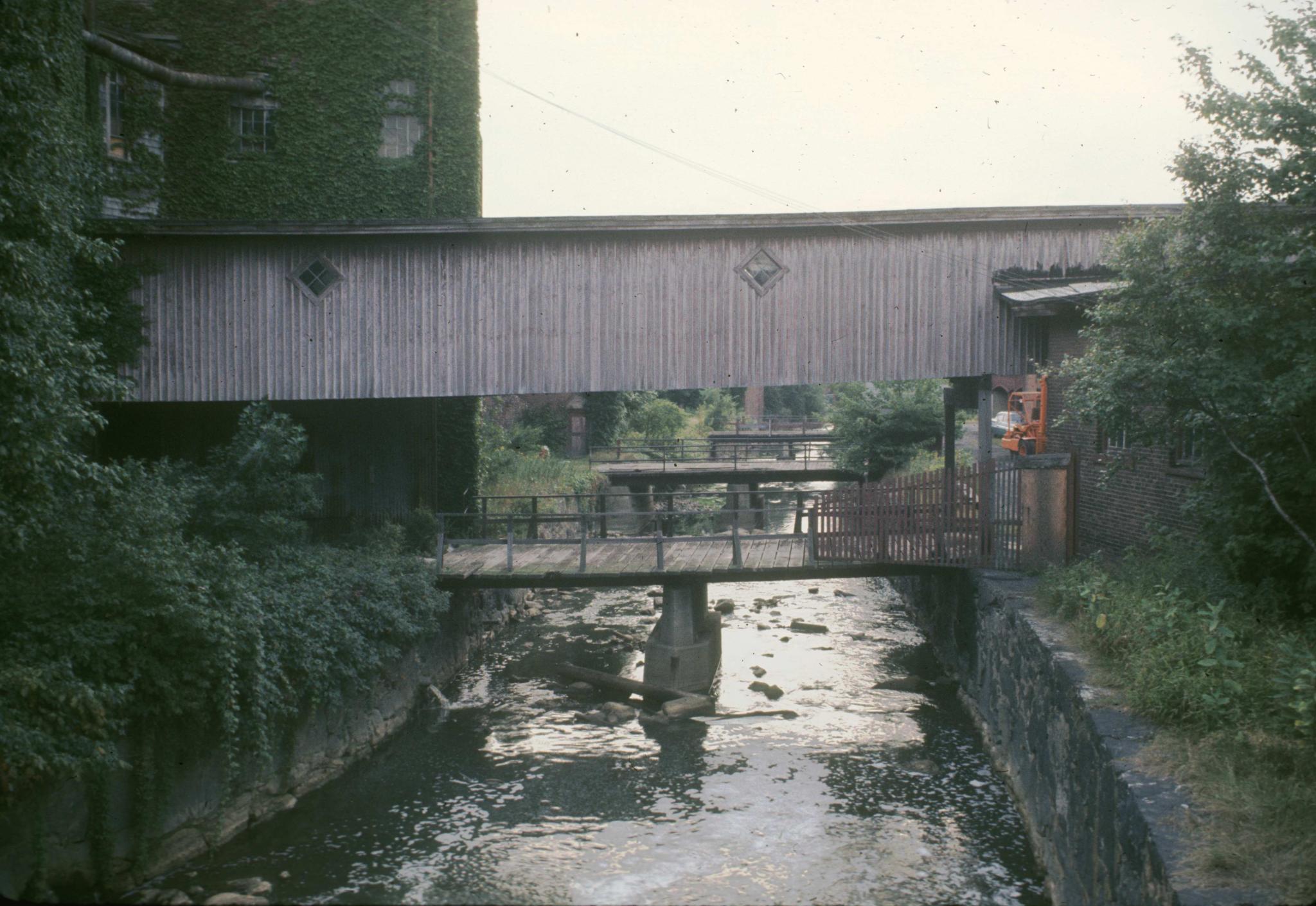 Photograph of the mill canal with an over-hanging enclosed pedestrian bridge…