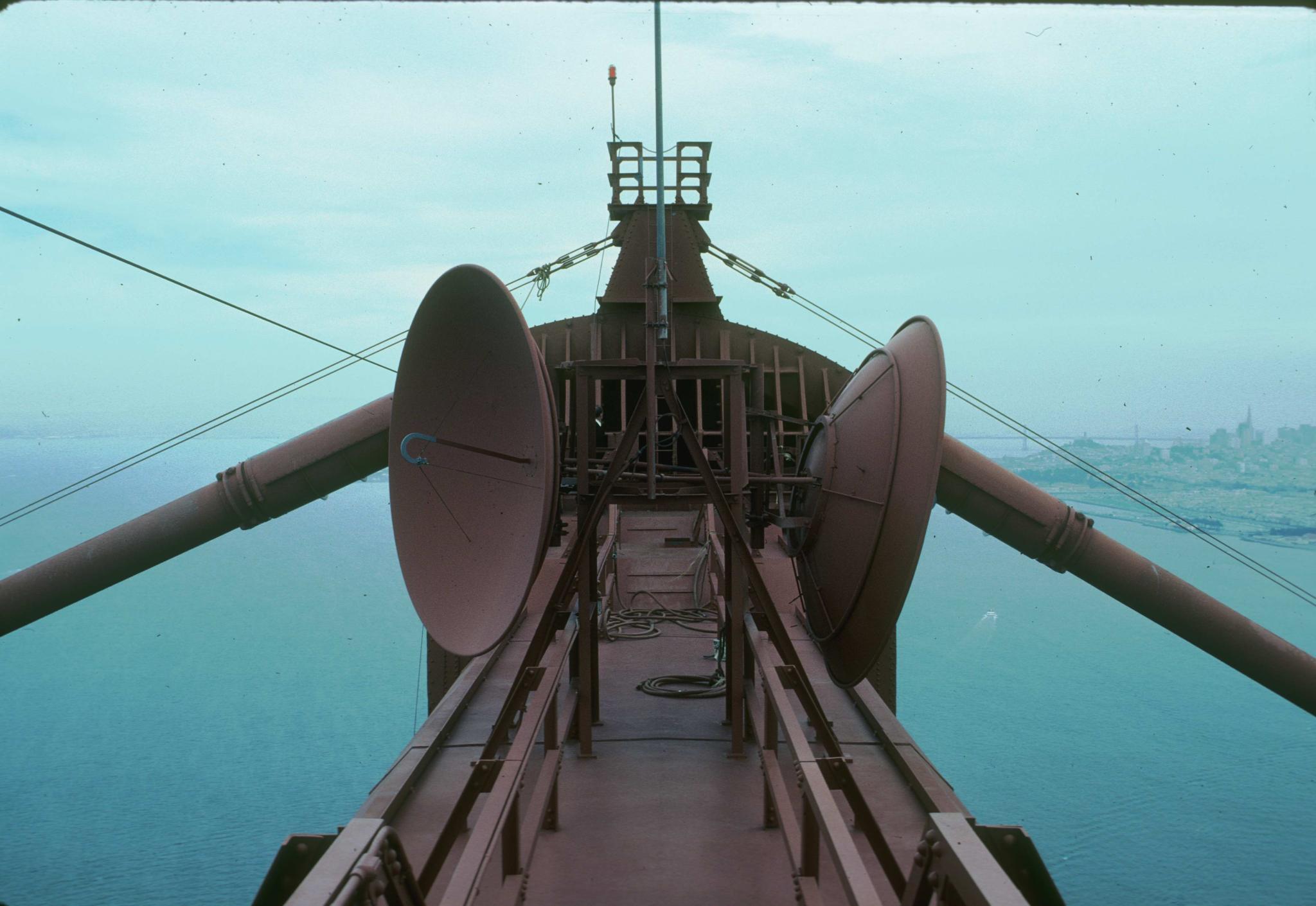 Photograph of Golden Gate Bridge saddle on top of tower.  The city of San…