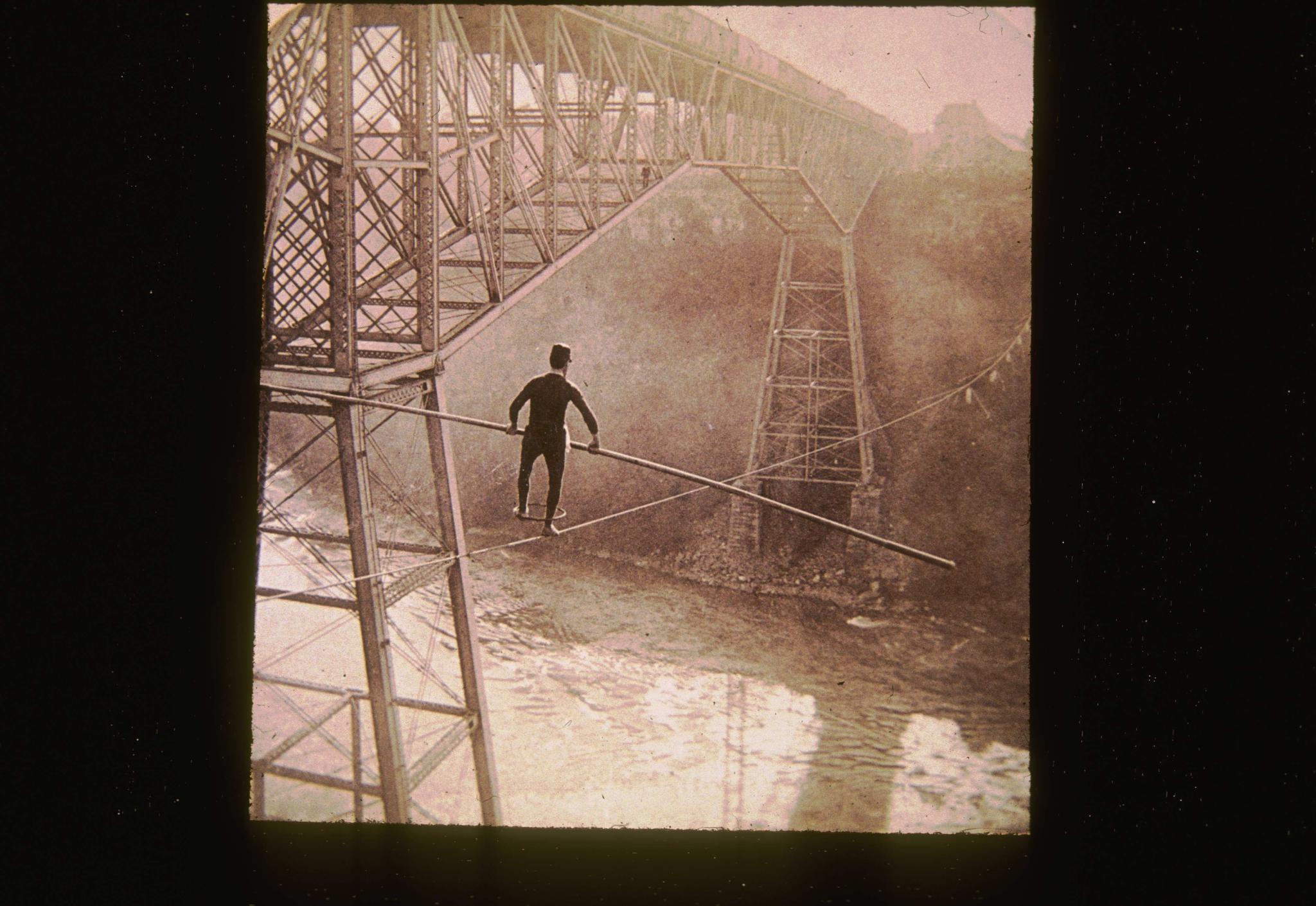 Historic photograph of a tight-rope walker over the Niagara gorge.  He is…