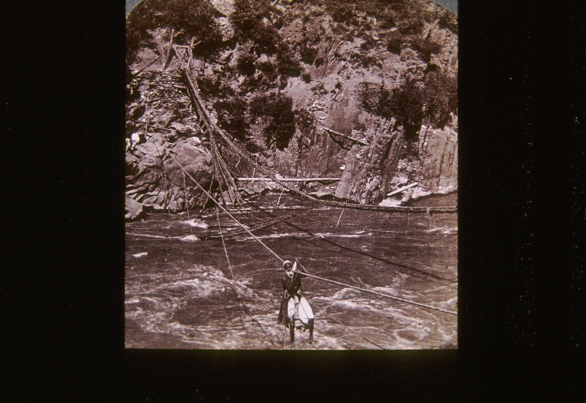 Unidentified primitive suspension bridge in India.  Bridge is crossing a…