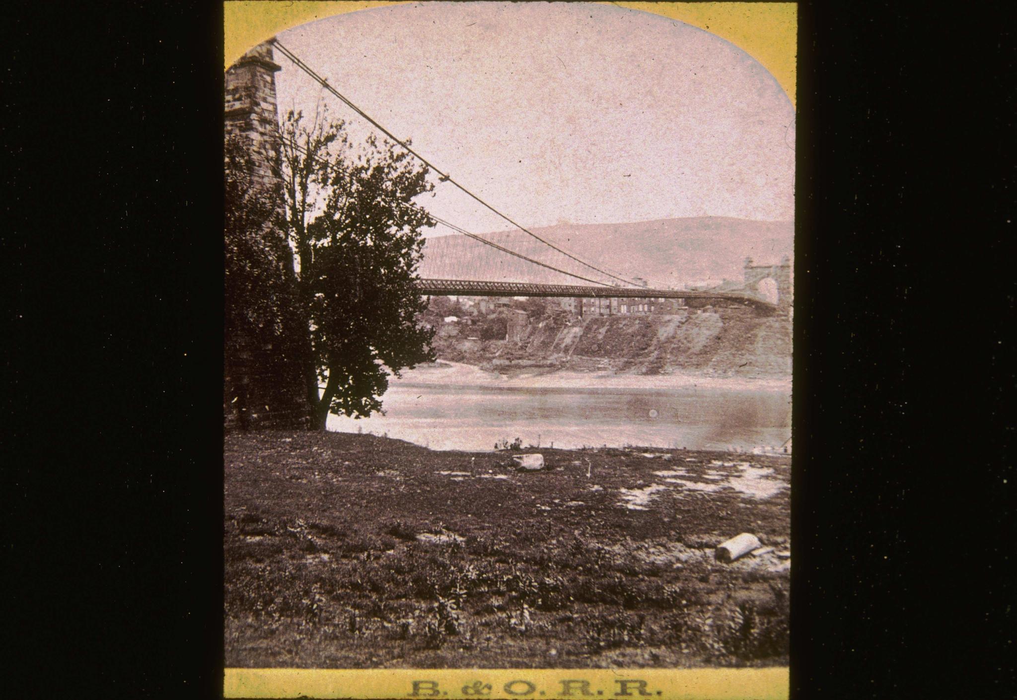 Historic photograph of the Wheeling Suspension bridge at an unknown date.  The…