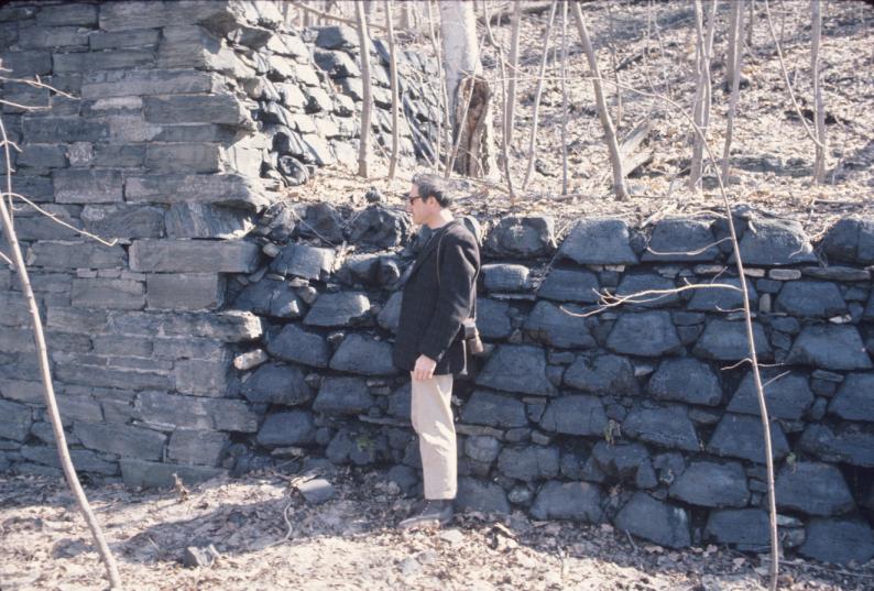 View of unidentified man in front of slag mold wall in forest.