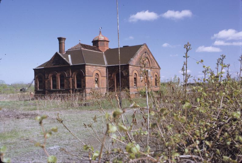 View of office building (listed as ca. 1881) across overgrown field.