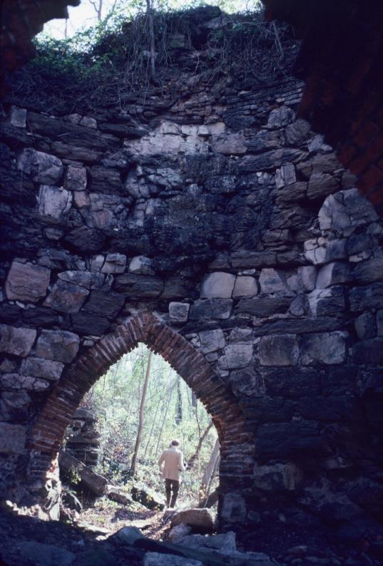 View of masonry furnace interior and brick arch looking out into forest.