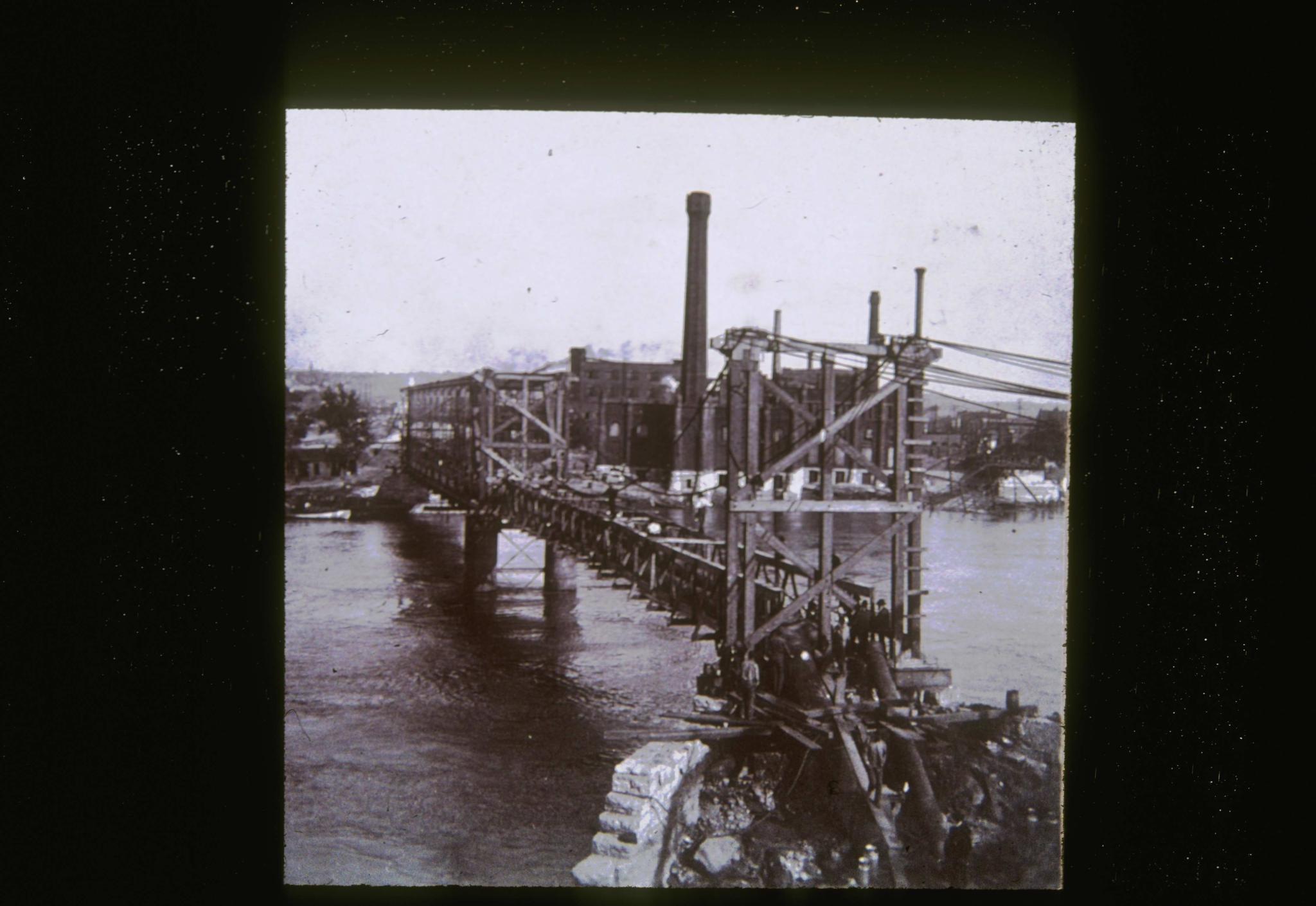 Historic photograph of an unidentified temporary suspension bridge.  The main…