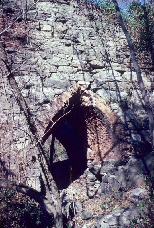 View of masonry blast furnace exterior and brick arch in forest.