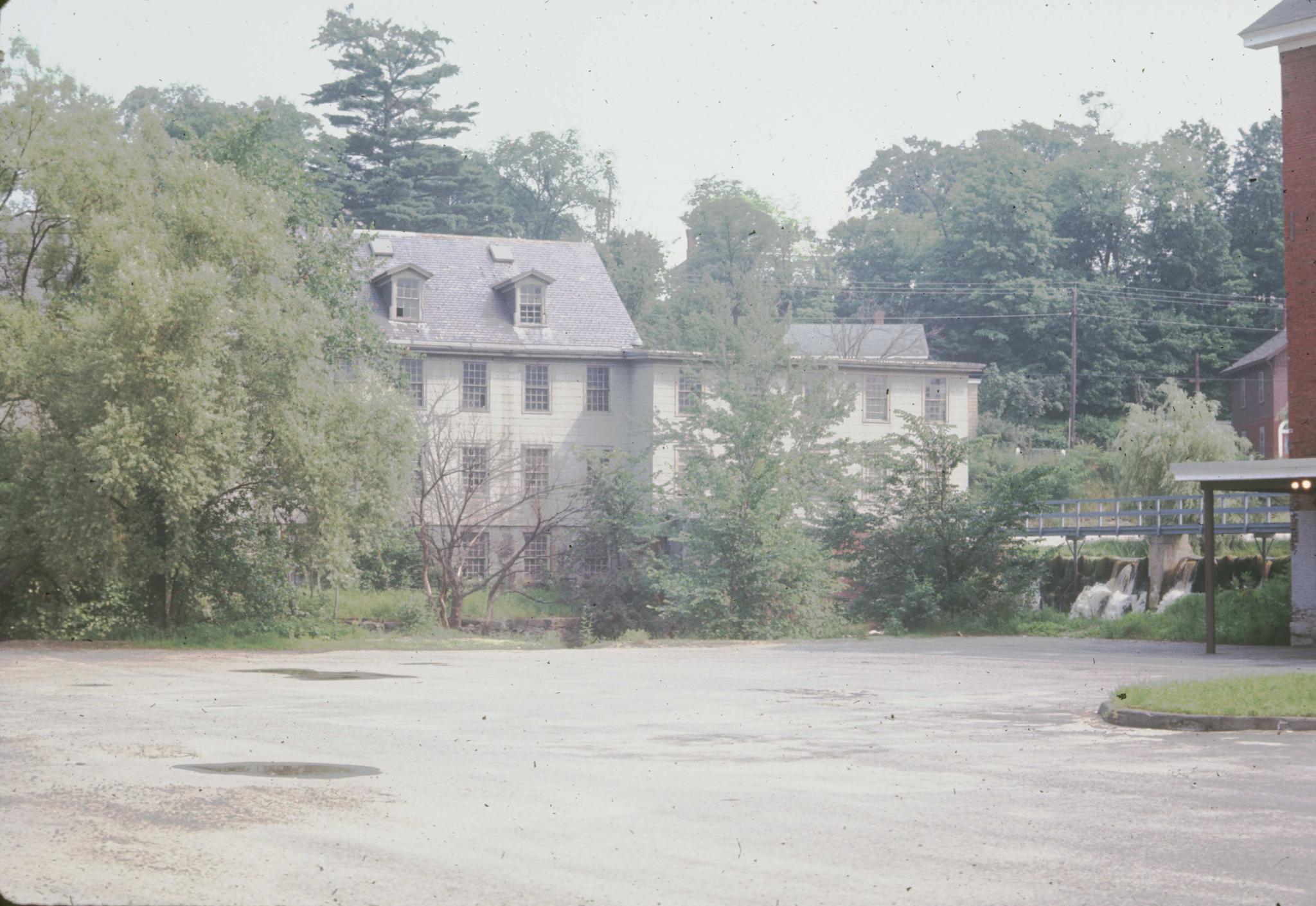 Photograph of mill buildings with the dam in midground at the right.