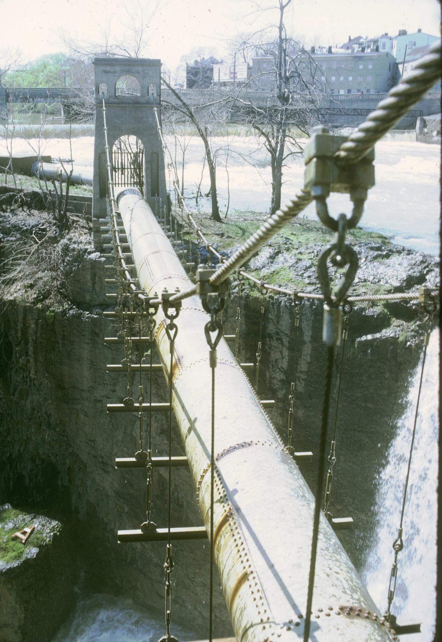 Photograph of an unidentified pipe suspension bridge crossing the falls of the…