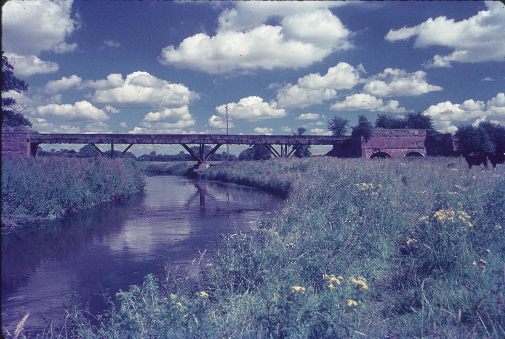 Iron aqueduct flume with brick abutments over a river and meadow. Longdon-upon-…