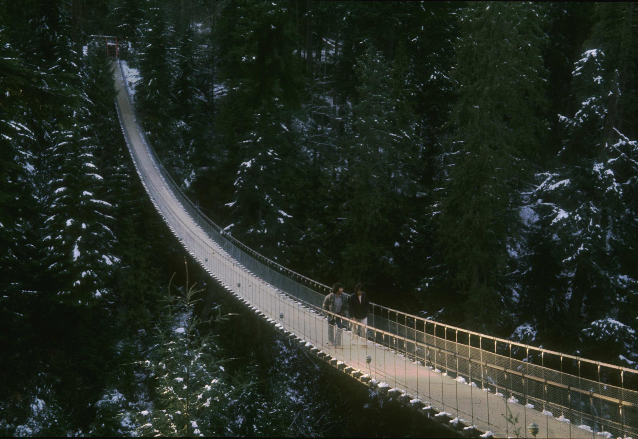 Photograph of two people crossing the Capilano bridge.  