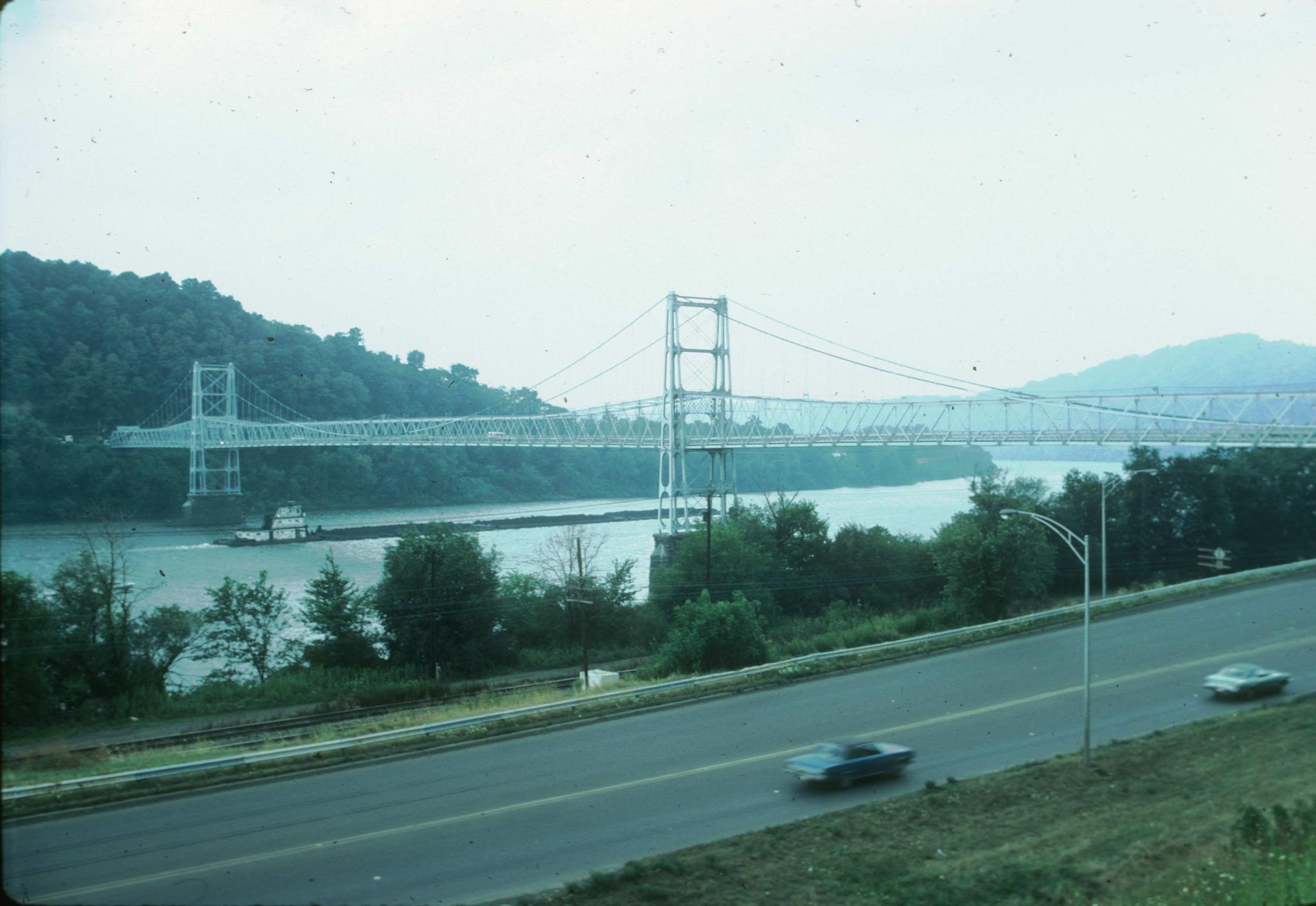 A wide view of the Newell Bridge.  A highway with two cars is in the foreground…