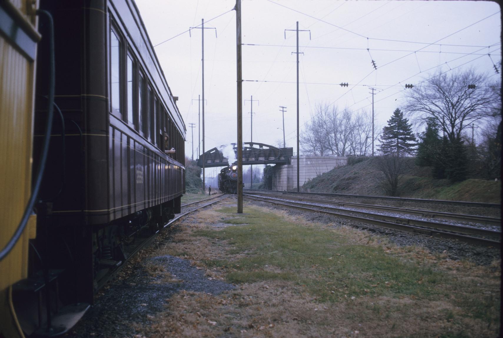 View of engine on PRR mainline passing passenger cars on siding