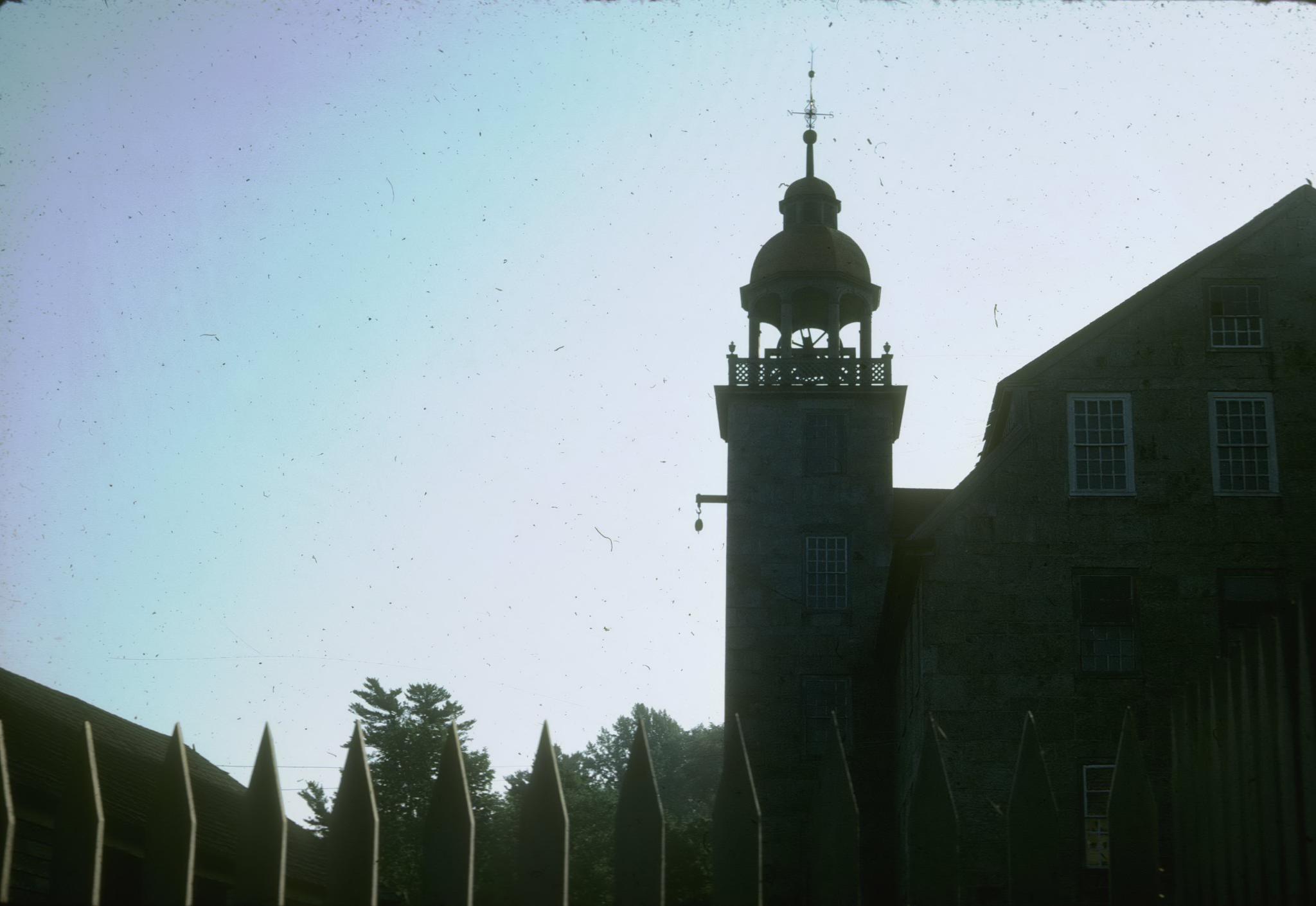 Photograph of the Crown Mill and its tower.  The mill is backlit and it is…