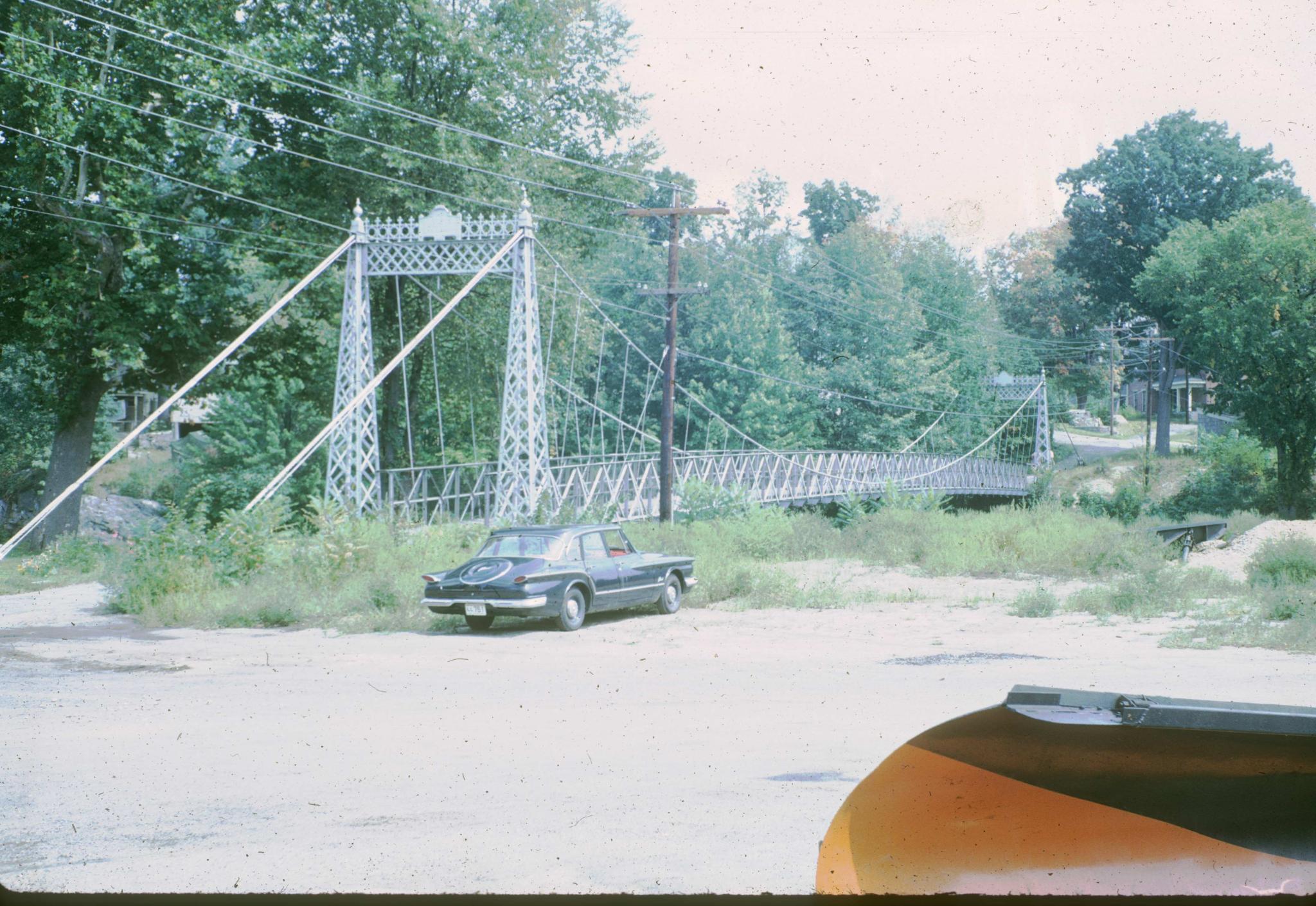 A three-quarters view of the suspension bridge with a car parked next to it.