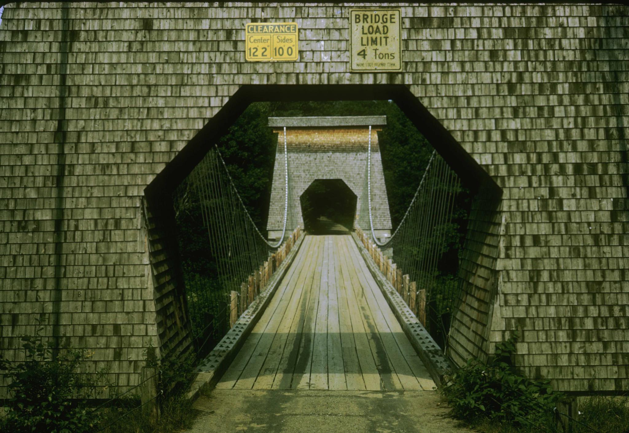 Photograph down the deck of the bridge framed by one of the covered support…