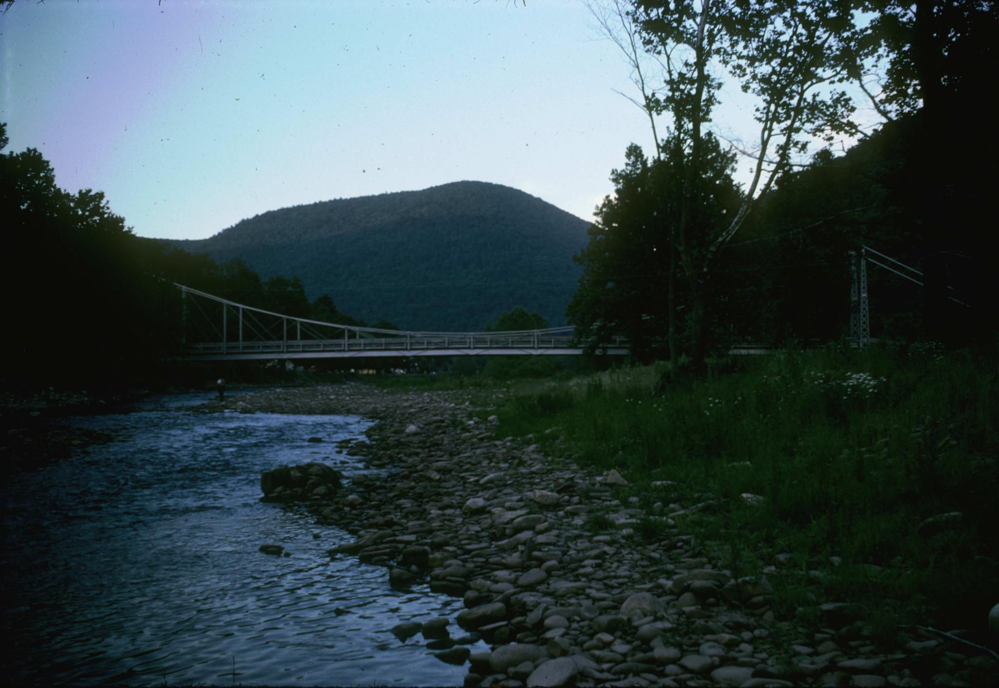 Photograph of the bridge taken from the river bank.  There is an angler in the…