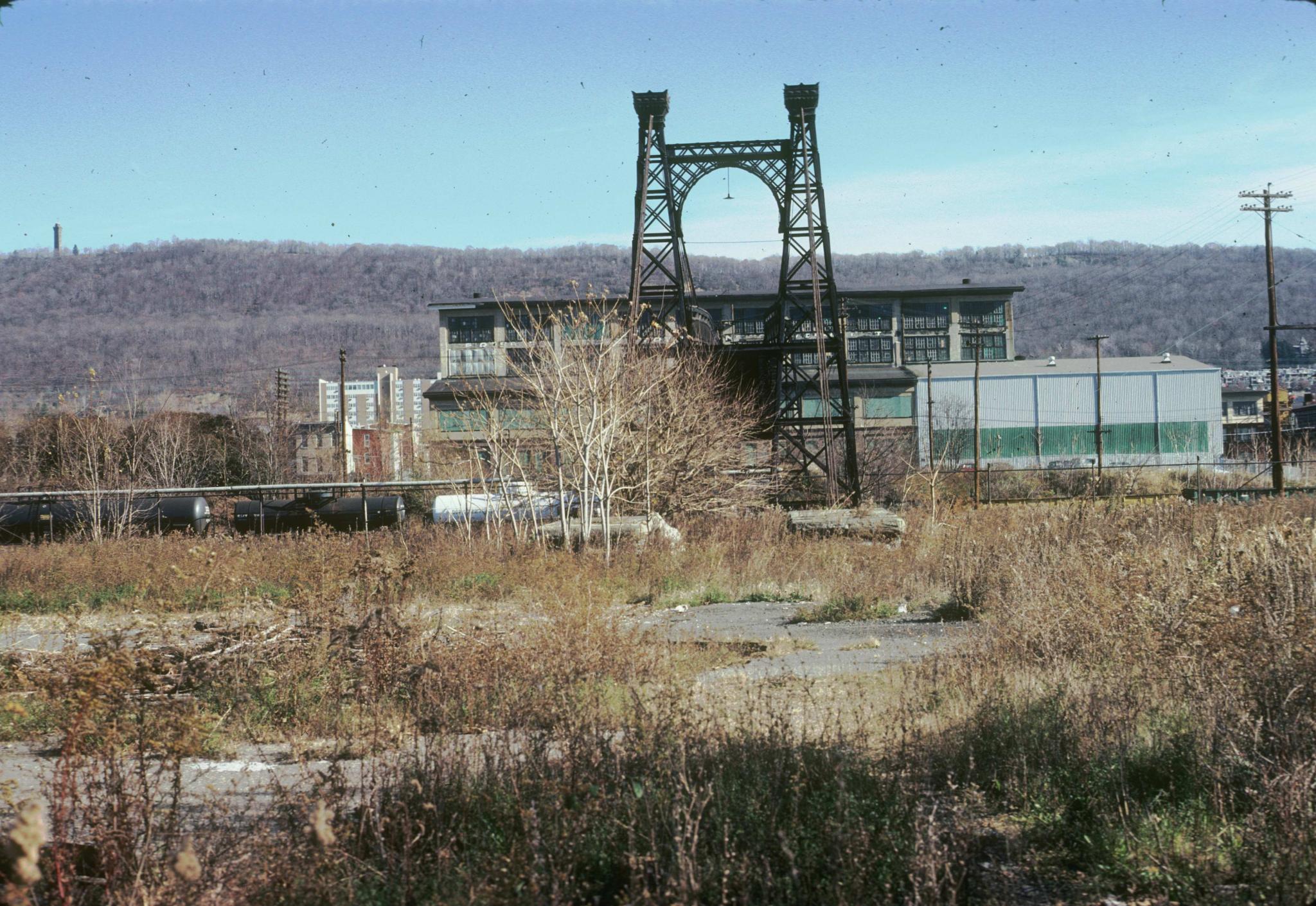 Photograph down the deck of the bridge.  Several tanker cars on the tracks are…