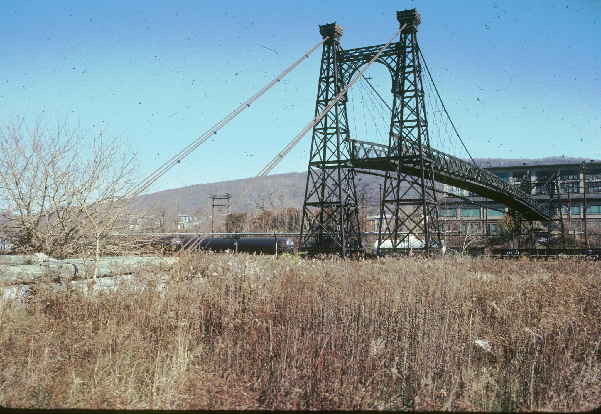 Photograph of the bridge with a line of tanker cars under it providing scale.